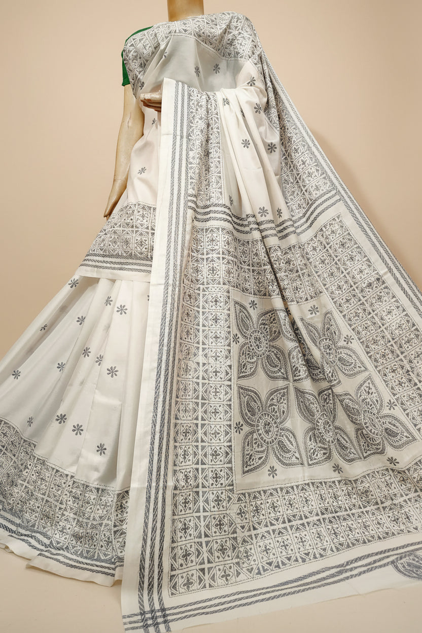 An off-white traditional Indian salwar suit set with detailed gray block prints and embroidery, displayed on a mannequin in a retail store setting with shelves of colorful folded garments in the background.