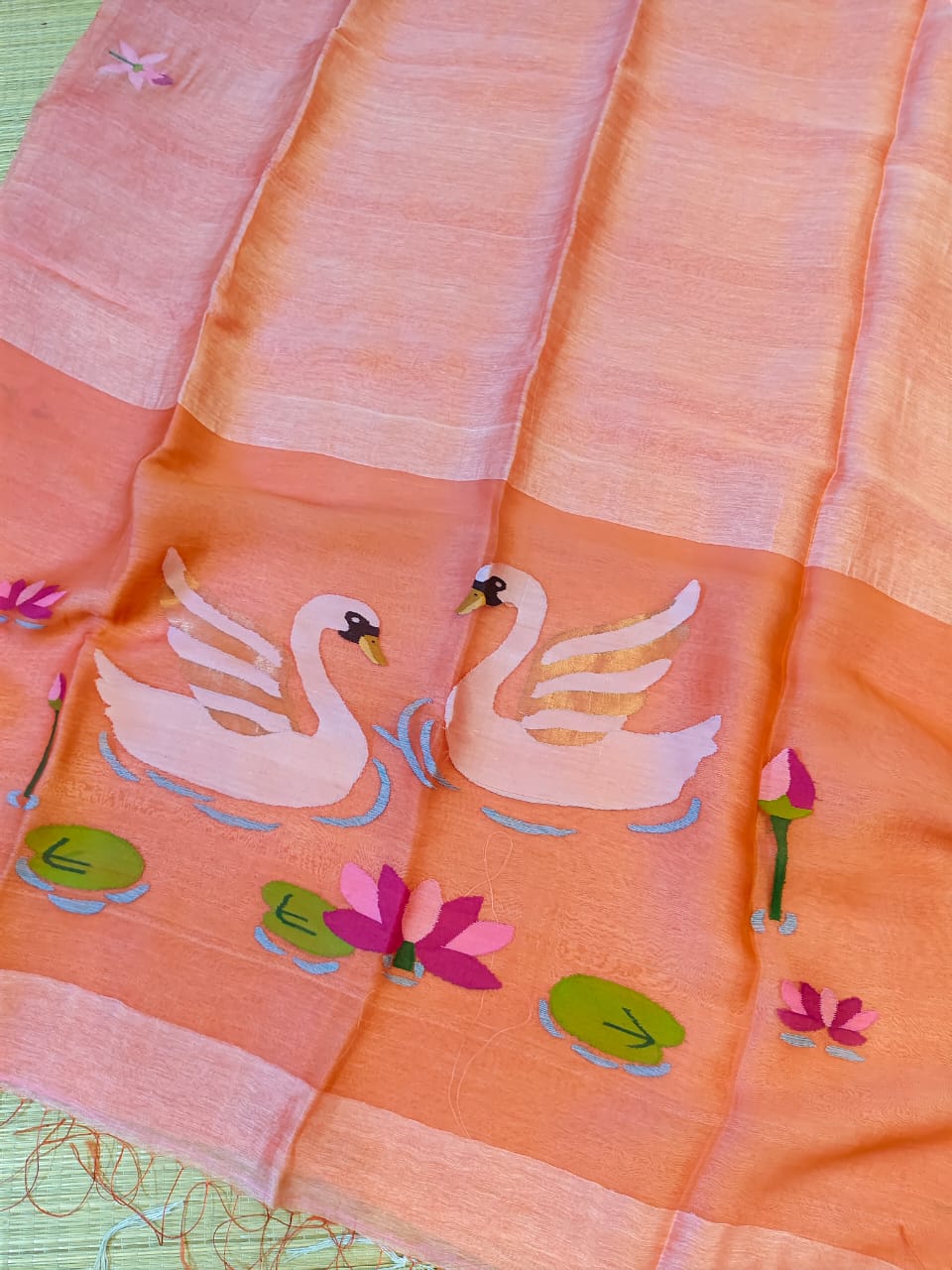 Orange fabric with white swan designs and pink flowers on a green background